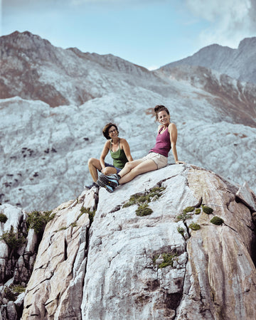 Zwei Frauen in nachhaltiger Funktionsunterwäsche von Ein schöner Fleck Erde sitzen entspannt auf einem Felsen in den Alpen – Naturverbundenheit und Outdoor-Lifestyle