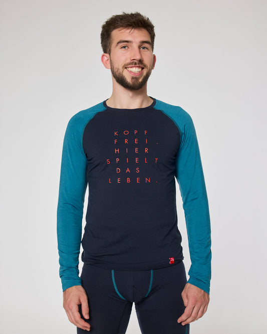 Mann trägt dunkelblaues Funktionsshirt mit türkisfarbenen Ärmeln von Ein schöner Fleck Erde, roter Schriftaufdruck ‚Kopf frei. Hier spielt das Leben.‘, kombiniert mit passender Funktionshose.