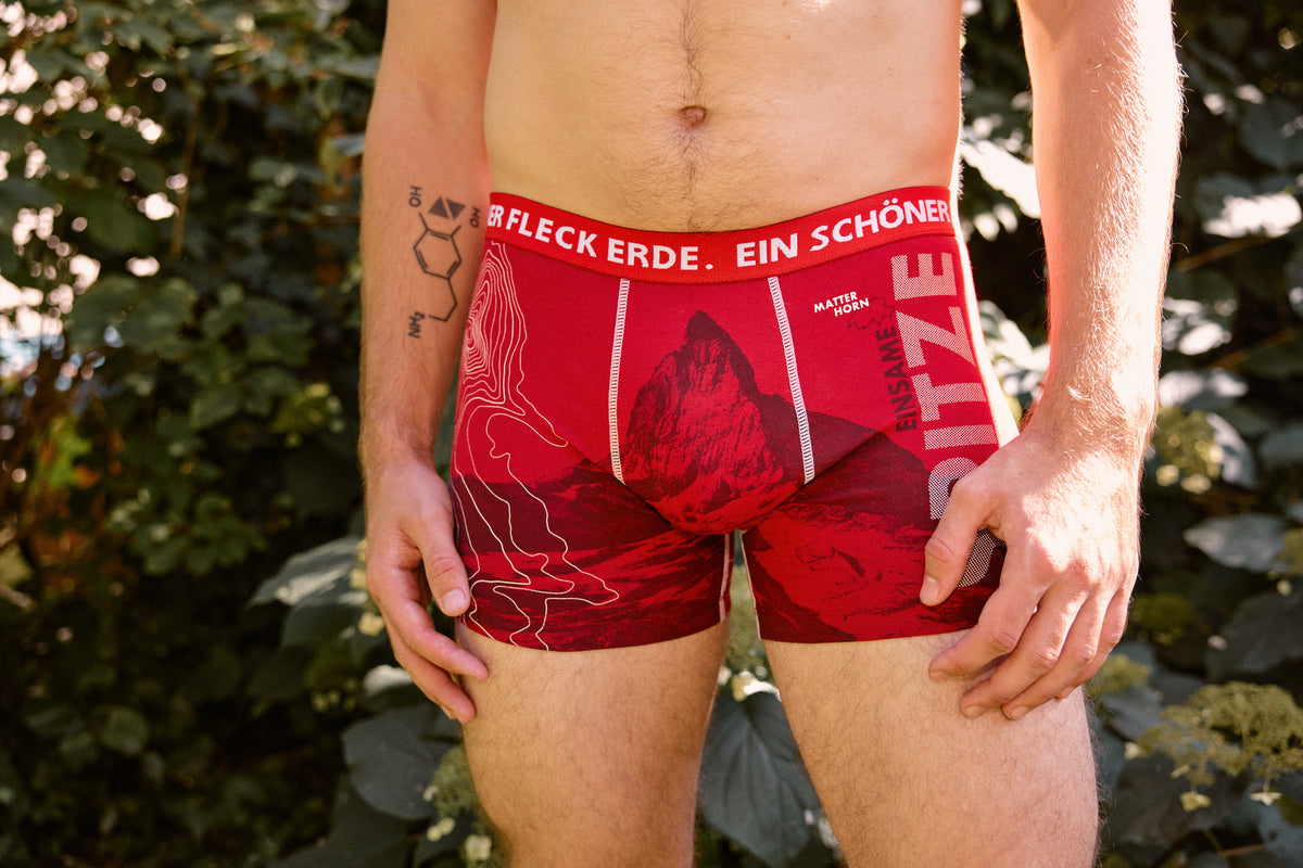 Rote Herren-Boxershorts mit Matterhorn-Motiv und Aufdruck ‚Einsame Spitze‘ von Ein schöner Fleck Erde im Natur-Outdoor-Setting