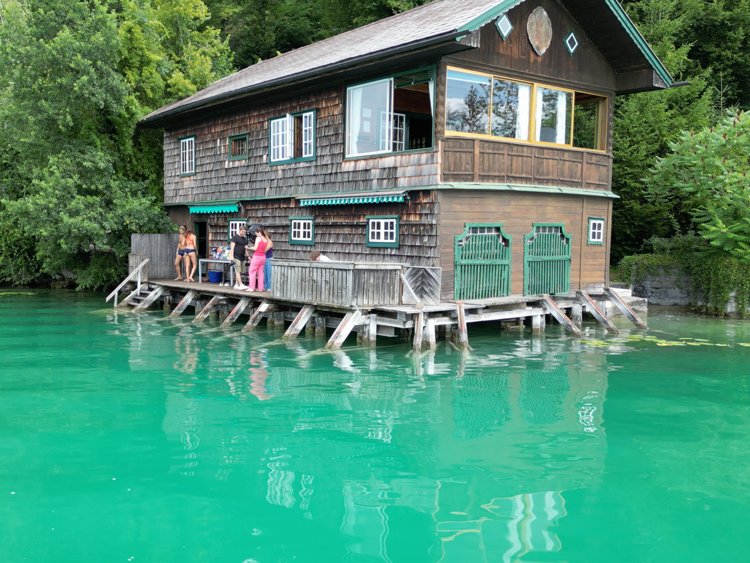 Holzhaus am türkisgrünen See mit Menschen auf dem Steg bei einem Fotoshooting für Ein schöner Fleck Erde