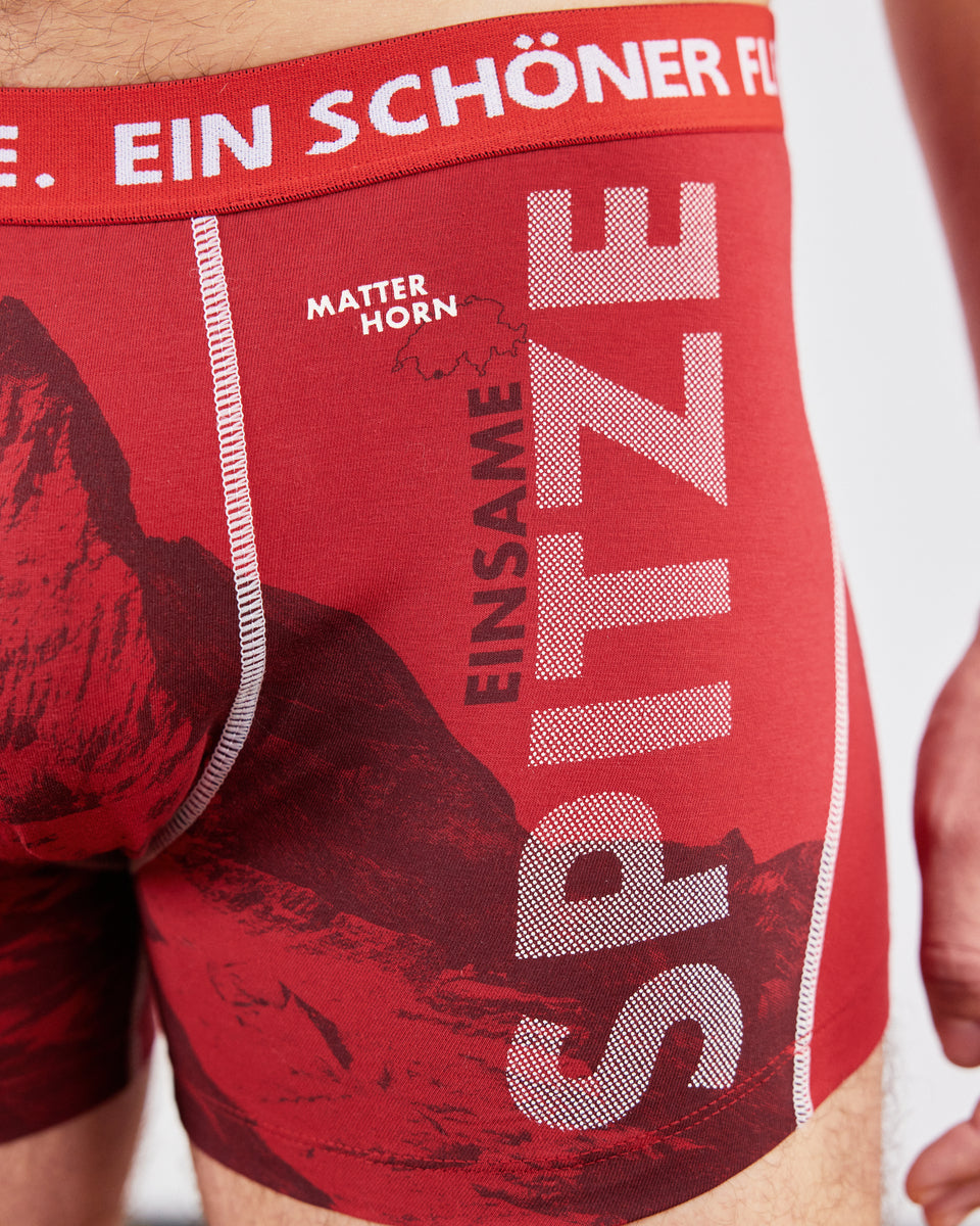 Rote Herren-Boxershorts mit Matterhorn-Motiv und Aufdruck ‚Einsame Spitze‘ von Ein schöner Fleck Erde