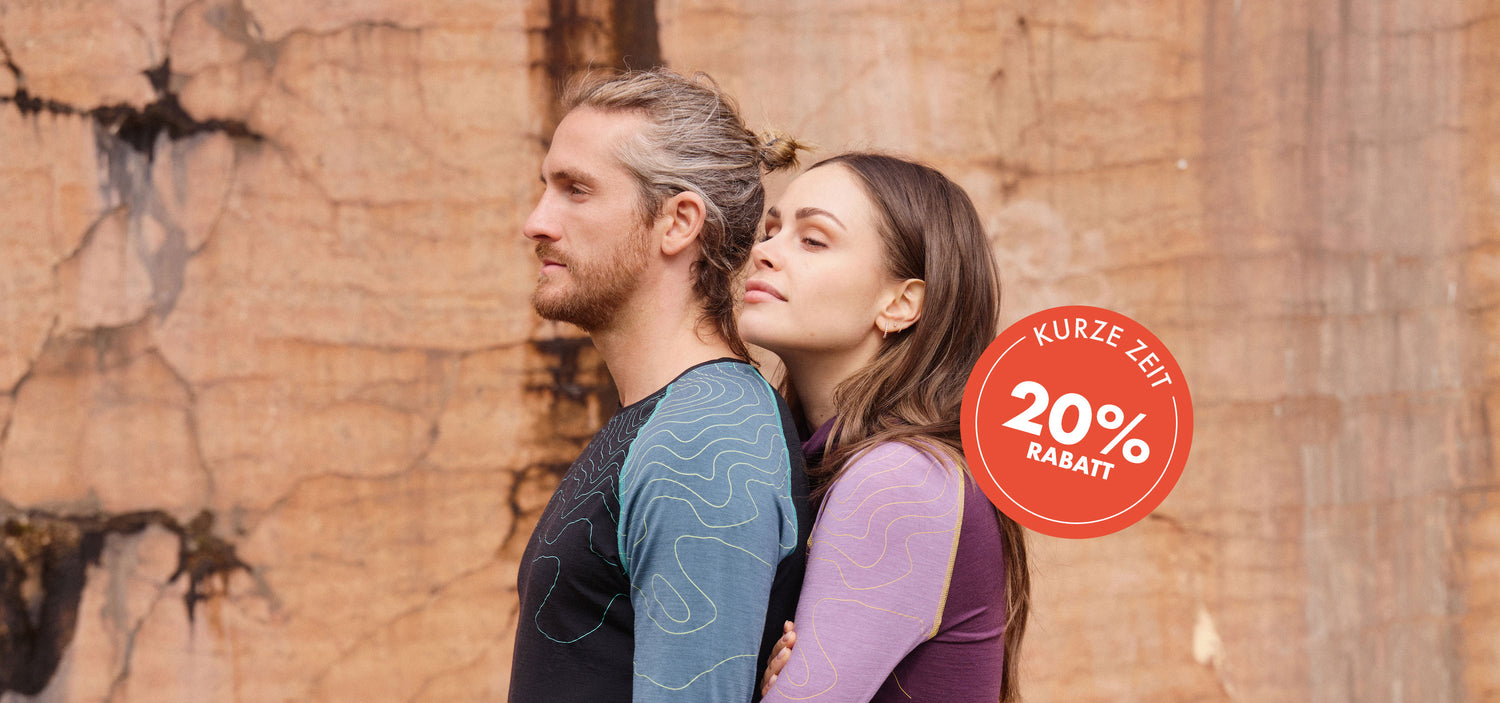 Zwei Personen tragen farbige Funktionsshirts vor einer Felswand; links ein blau-schwarzes Shirt mit Linienmuster, rechts ein lila-gelbes Shirt.